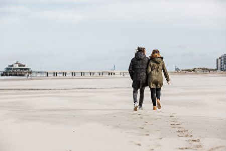 Paar in winterlicher Kleidung läuft über den Strand in Richtung Pier.