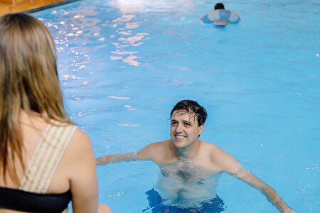 Mann im Wasser mit Frau am Beckenrand