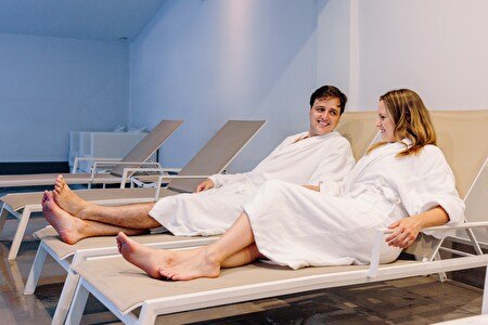 Paar im Bademantel auf Liegestuhl neben dem Pool